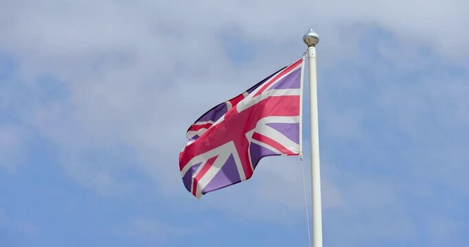 Slow motion footage of a British UK Union Jack Flag flag blowing in the wind on a sunny summers day with a blue sky and a few white clouds