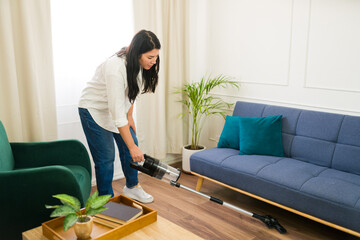 Caucasian woman cleaning her cozy living room with a handheld vacuum on a sunny day at home