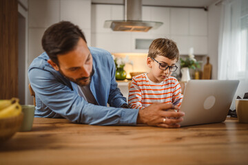 Father and son buy online with credit card on laptop in the kitchen