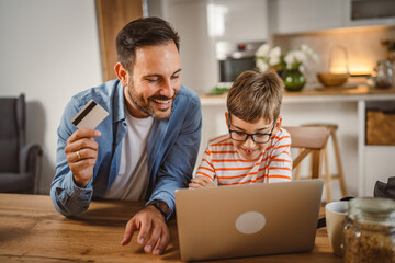 Father and son buy online with credit card on laptop in the kitchen