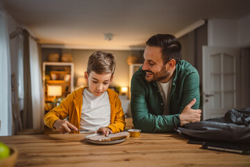 Fototapeta premium Young boy smear pate on bread while dad pack his backpack for school