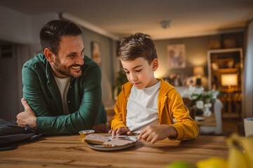 Young boy smear pate on bread while dad pack his backpack for school