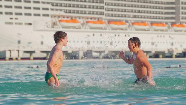 4k, A view of two boys children splashing, playing in water, in the background cruise ship, Sir Bani Yas, United Arab Emirates