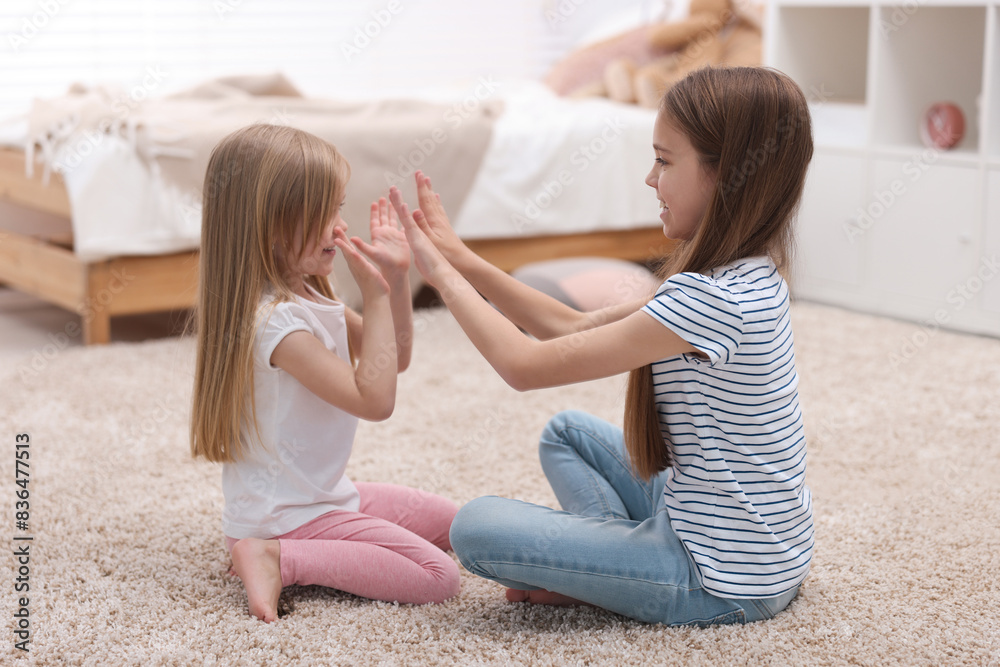 Poster Cute little sisters playing clapping game with hands at home