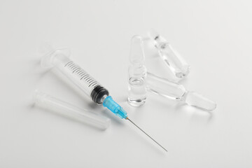 Glass ampoules with liquid and syringe on white background, closeup