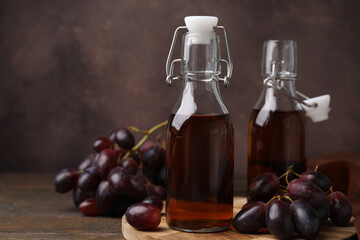 Bottles with wine vinegar and grapes on wooden table, closeup. Space for text