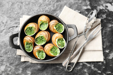 Delicious cooked snails in baking dish served on grey textured table, flat lay