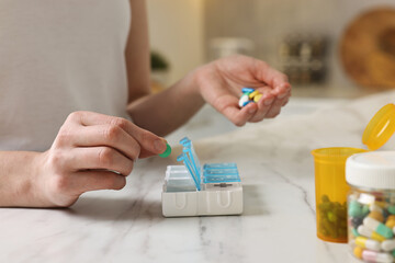 Woman with pills and organizer at white marble table, closeup