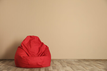 Red bean bag chair on floor near beige wall indoors, space for text