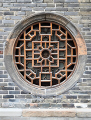 A Chinese style circle window with carved patterns on the brick wall, traditional wooden windows and round frames
