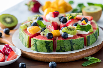 A watermelon pizza topped with cream cheese and fresh fruit pieces.