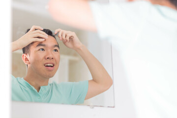 A teen boy is combing his hair while looking at himself in the mirror