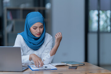Cheerful muslim lady wear hijab working in the office, using laptop, Side view of smiling arab woman, freelancer typing on laptop, Muslim working woman concept.