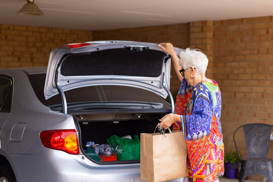 elderly lady taking brown paper bag of groceries out of car boot