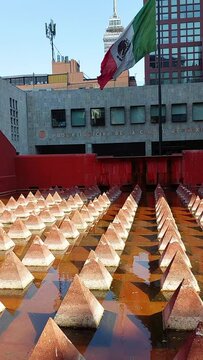 Patio con espejo de agua y bandera mexicana  ondeando al viento con fachada edificio Poder Judicial de la Ciudad de Mexico.