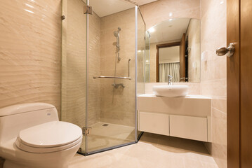 a modern bathroom with beige tiles, a glass shower enclosure, a white toilet, a sink cabinet, a mirror, a towel rack, and chrome fixtures, creating a clean and simple atmosphere.