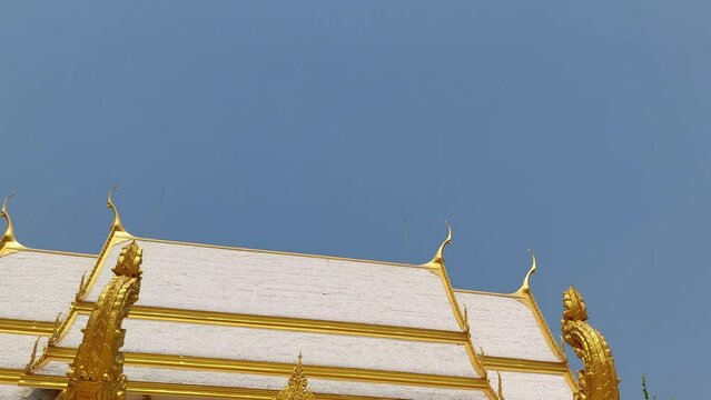From an angle on the roof of the church, a chofha slowly emerges to reveal a delicate, golden pointed tip.  Then look at the beautiful building and stairs with the twin Nagas.4k,pattaya,chonburi,thail