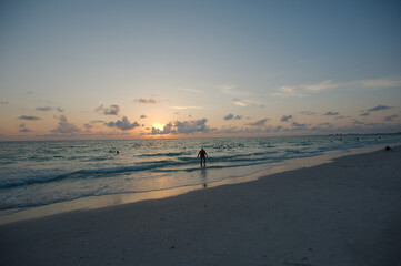 Sunset at Pass-a-grille Beach in St Petersburg Florida. Low light with multiple people in the water. Golden glow and blue sky of the Sun in the background. Horizontal View. Cloudscape landscape.
