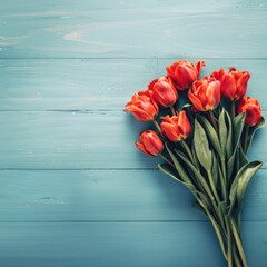 Red tulips with green leaves tied with a red ribbon on a blue wooden background. Flat lay composition with copy space. Spring celebration and romantic gesture concept.
