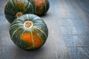 Green and orange small pumpkins on a gray-blue wooden table, space for text, minimalism.