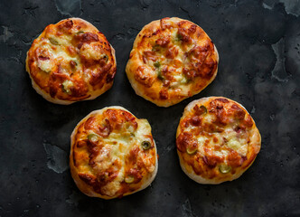 Mini pizza with ham, olives and mozzarella - a delicious snack, tapas on a dark background, top view