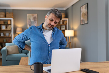 Shot of a businessman suffering from a backache while working at his desk in his office. Man having...