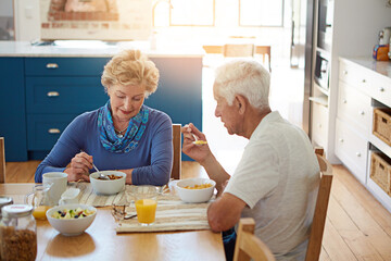 Senior, couple or talking with eating at breakfast in dining room for nutrition, healthy meal or retirement. Elderly, people or porridge in home with conversation, relax or morning routine at table