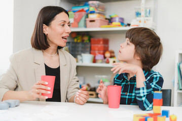 Obraz premium Beautiful woman speech therapist teaches boy the correct pronunciation of words and sounds in the office