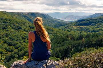 Naklejka premium Woman sitting on rock enjoying mountains and forest view