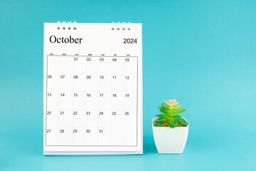 2024 October desk calendar and plant pot on blue background.