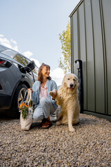 Young woman with her cute white dog sitting together, arrived home by electric vehicle with fresh...