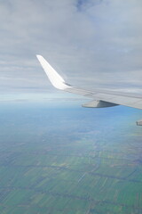 A white airplane wing is flying over a green field