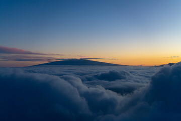 Aerial photo of Mauna Loa and Mauna Kea above the clouds at sunset. Flight from Hilo to Honolulu.