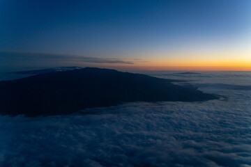 Aerial photo of Mauna Loa and Mauna Kea above the clouds at sunset. Flight from Hilo to Honolulu.