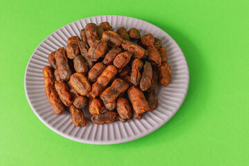 Sweet, spicy tamarind tree fruit in round plate on green background