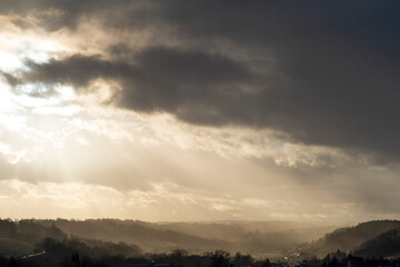 Fototapeta premium Sun shining behind the stormy skies in a dimly lit pasture