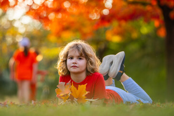Cute blonde child rest on autumn park. Child play with autumn fall leaves. Kid laying down on the...