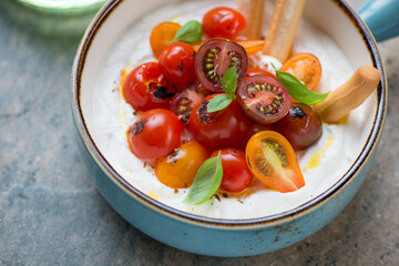 Ricotta dipping sauce with roasted tomatoes, grissini and basil in a turquoise serving bowl, middle...