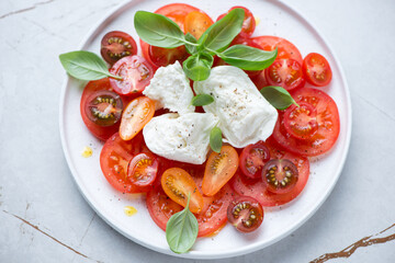 Caprese with buffalo mozzarella, tomatoes and green basil leaves served on a white plate, horizontal shot, elevated view