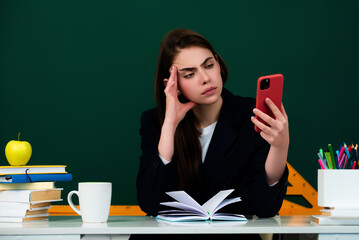 Female student using phone in classroom. School girl chatting on mobile phone near blackboard....