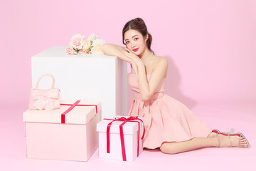 Portrait of cute Asian woman in pink dress gesture feeling surprise happiness with valentine or birthday gift on isolated background. Female model holding present boxes and strawberry cake.