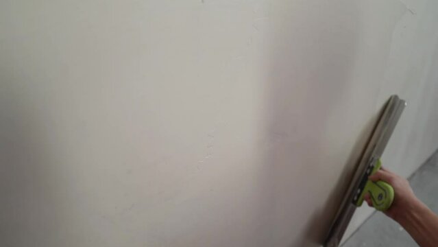 The process of putty the walls with a large spatula. The worker covers the uneven walls, man's hands with a large spatula and putty, apartment repair. Puttying the wall with a large spatula.