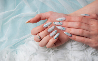 Female hands with blue nail design on blue silk background.