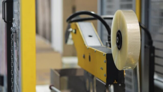 Automated carton sealing machine taping cardboard boxes on conveyor line.