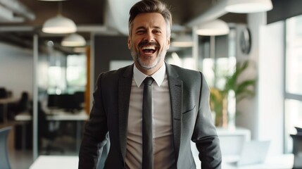 Fototapeta premium Confident businessman in a suit laughing in a modern office with a bright, open layout.