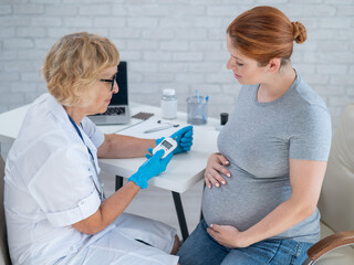 An elderly female doctor checks the blood sugar level of a pregnant red-haired woman. Gestational diabetes. 