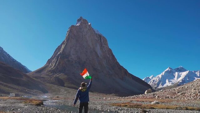 Rear View shot of an Indian flag waving the flag of India in front of Gonbo Rangjon mountain at Zanskar in Ladakh, India. Man waves Indian flag in the mountains. Patriotic Indian man waving flag.