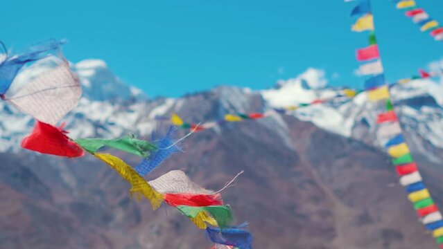 Slow motion shot of Buddhist prayer flags waving in the wind in front of the snow covered Himalayan mountain peaks as seen from Padum in Ladakh, India. Religious prayer flags wave against the blue sky