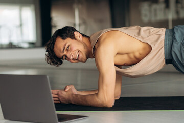 Happy athletic young man in sportswear stretching his body at home. Sporty man doing yoga plank...