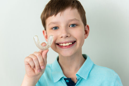 Smiling child boy over gray background holding an invisible aligner ready to use it. Dental healthcare and confidence concept